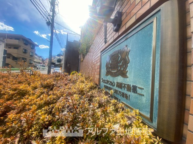 ライオンズマンション高幡不動第二の庭|陽射しに映えるエントランスのプレートが、品格ある佇まいを演出。周囲の緑と調和し、落ち着いた住環境が広がります。快適な暮らしを叶える、魅力的なマンションです。