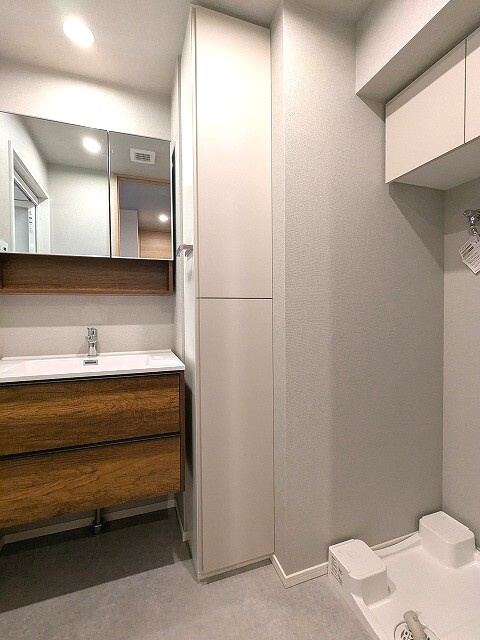 ミリアレジデンス蔵前の洗面所|トイレと独立した2面鏡付洗面台、洗面台下にヘルスメーターストックあります、洗濯機置場はお手入れし易い様に排水口を手前中央に配置し、足高の防水パンです