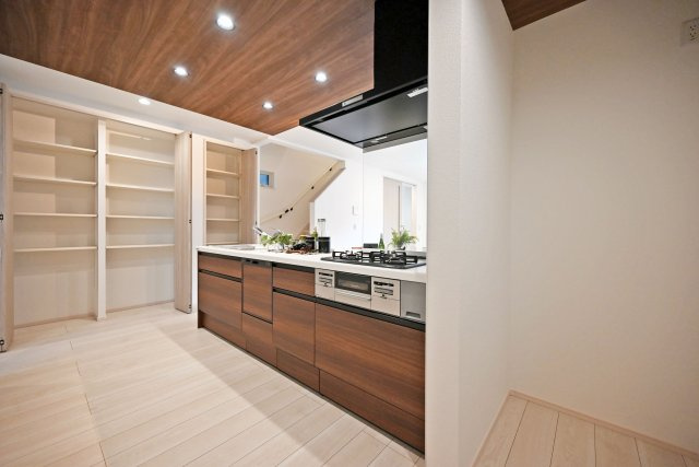 尼崎市東園田町7丁目新築一戸建て│2LDK+2S│並列駐車2台可のキッチン|1階キッチン奥側から撮影した写真です。コンロ前は視界を確保した耐熱パネル使用。コンロはもちろんガラストップ施工で掃除がらくらく！キッチン左側には可動棚式大容量の収納庫が設けられています。