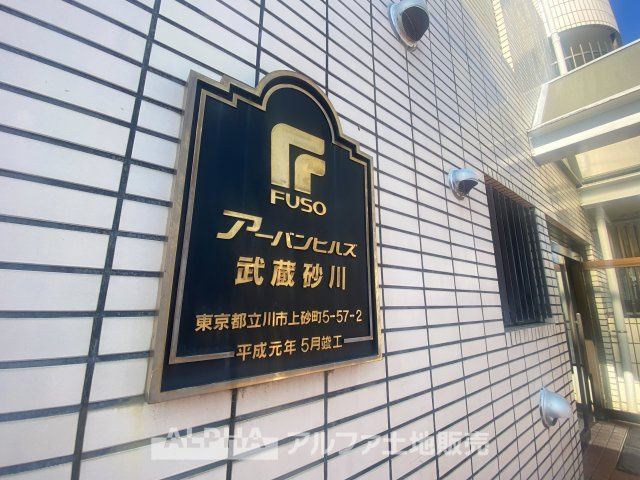 アーバンヒルズ武蔵砂川町の外観|陽射しに映えるエントランスのプレートが、品格ある佇まいを演出。周囲の緑と調和し、落ち着いた住環境が広がります。快適な暮らしを叶える、魅力的なマンションです。