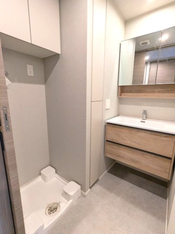ミリアレジデンス蔵前の洗面所|トイレと独立した2面鏡付洗面台、洗面台下にヘルスメーターストックあります、洗濯機置場はお手入れし易い様に排水口を手前中央に配置し、足高の防水パンです