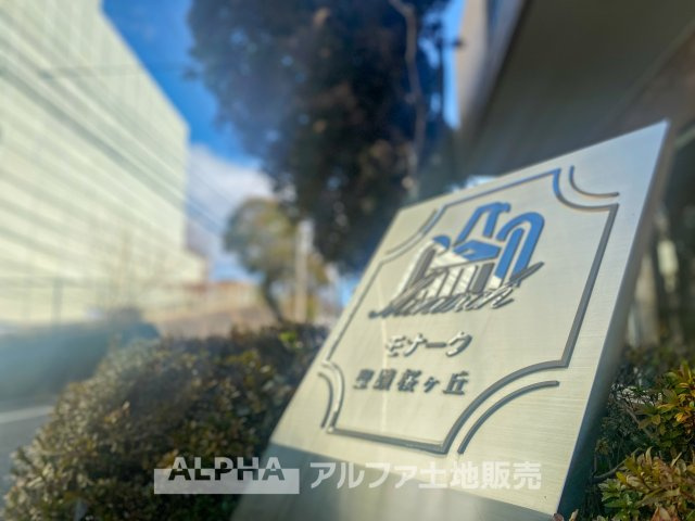 モナーク聖蹟桜ヶ丘の外観|洗練されたデザインの館銘板が、住まいの品格を引き立てます。緑に囲まれたエントランスが、帰宅するたびに心安らぐ空間を演出。陽光に映えるデザインが、住む人の誇りを感じさせるエントランスのアクセントに。