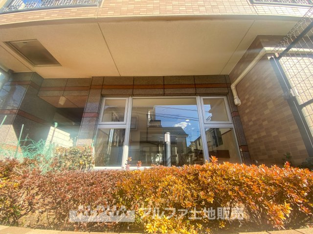 モナーク聖蹟桜ヶ丘の外観|植栽が彩るエントランス周り。大きな窓から自然光が差し込み、開放的な雰囲気を演出します。帰宅するたびに心地よさを感じられる、落ち着いた佇まいのマンション。