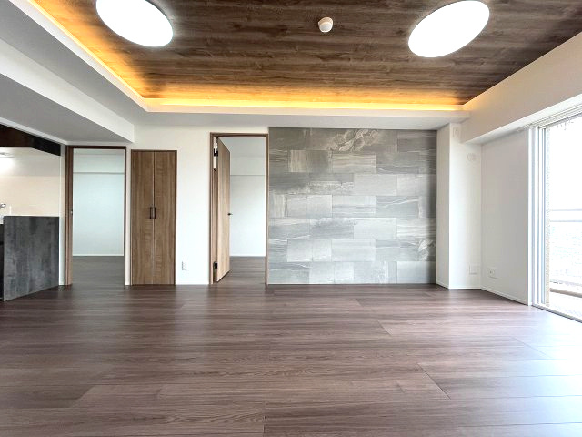 忠道マンションA棟の居間・リビング|壁一面に配された石目調のアクセントウォールが空間のモダンさを際立たせ、奥に見えるバルコニーからは光が差し込み、開放感にあふれています。