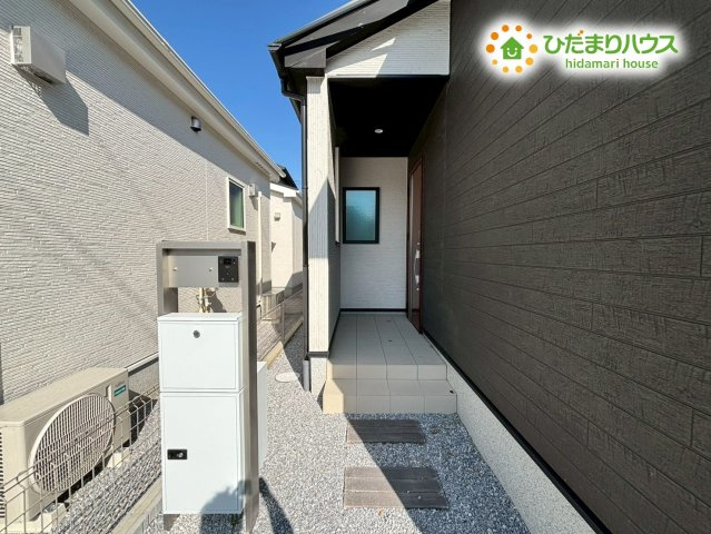 東松山市石橋　23-2期　新築一戸建て　リナージュ　02の玄関|玄関扉の前には屋根があり、雨の日でも慌てずに鍵を開けられます。ベビーカーや濡れた傘を一時的に置くのにも便利ですね。木目調のドアが白い外壁に映えていてとてもお洒落ですね。