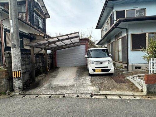 萩生　中古戸建の駐車場|シャッター車庫とカーポートを備えた機能的な外観。前面道路が6ｍと広いため、お家全体がゆったりと余裕を持って見えます。駐車スペースは3台以上確保されており、ご友人が遊びに来た際も笑顔で迎えられる住まい。