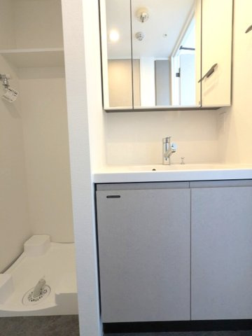 LUMIEC un 入谷の洗面所|トイレと独立した三面鏡付・ハンドシャワー付洗面台、洗濯機置場は排水溝のお手入れをしやすく手前中央に配置し、足高の防水パンです