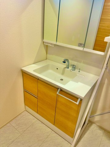 ブルーミングガーデン西原町小那覇・１号棟の独立洗面台|水ハネ軽減やコップ置場等として通常よりもワイドなハンドシャワー＆三面鏡付き洗面化粧台