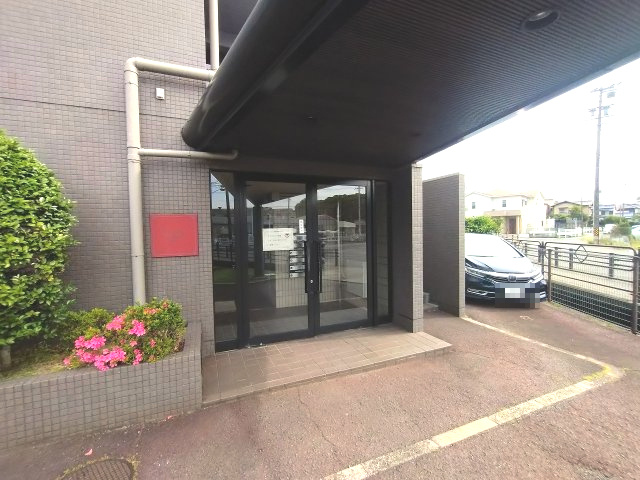 ユニーブル漆山のエントランス|ダークトーンで統一されたシックなエントランス。植栽の緑と鮮やかなピンクの花が彩りを添え、訪れる人を温かく迎えます。