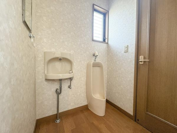 荏隈　中古のトイレ|窓があり通気性に配慮されたトイレです。床材と壁紙の組み合わせが落ち着いた印象を与えます。手洗い器と小便器が設置されています。ドアの開閉もスムーズです。照明の明るさも十分です。