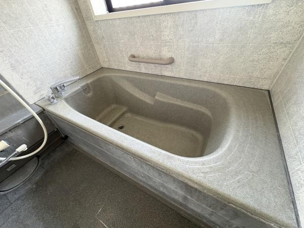 荏隈　中古の浴室|ゆったりとしたサイズ感のバスタブが特徴です。壁面には手すりが備え付けられており安心して利用できます。窓があるため換気や採光にも配慮された設計です。床や壁も落ち着いた色合いでまとまっています。