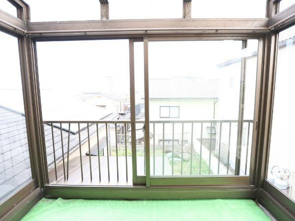 葛木　中古のバルコニー|明るい日差しが差し込むバルコニーです。ガラス窓に囲まれており風や雨を気にせずに過ごせます。視界が広がる開放的な空間となっています。床にはグリーンのマットが敷かれており雰囲気が柔らかくなっています。