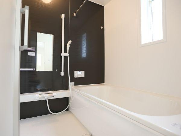 挾間町下市第1-4号棟の浴室|モダンな配色が特徴のバスルームです。窓からは自然光が入り空間に明るさをもたらします。壁面のダークカラーと白のコントラストが印象的です。ミラーや手すりも備わっており機能性も感じられます。