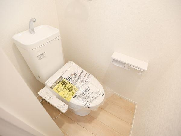 挾間町下市第1-4号棟のトイレ|温水洗浄機能付き便座が設置されています。明るい色合いの床材が採用されお手入れも簡単です。トイレットペーパー収納が壁付けで設置されています。清潔感のある空間が広がっています。