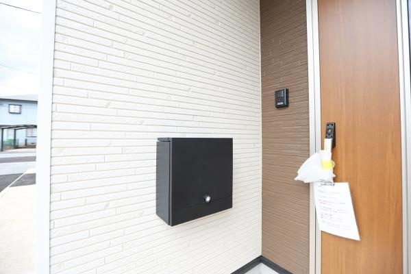 挾間町下市第1-3号棟の玄関|シンプルでモダンなデザインの玄関が特徴です。壁の質感とカラーが落ち着いた印象を与えます。ポストとインターホンが使いやすい位置に配置されています。玄関ドアは木目調で雰囲気が調和しています。