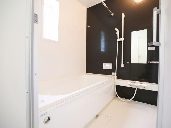 挾間町下市第1-2号棟の浴室|明るい色合いとシックなアクセントパネルが特徴のバス。洗い場が広くゆったりとした空間が確保されています。ワイドミラーと手すり付きで使い勝手にも配慮されています。換気もしやすい窓付きです。