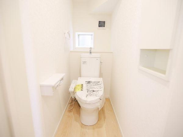 挾間町下市第1-2号棟のトイレ|明るい色合いと清潔感のあるトイレです。小窓からの採光で空間がより開放的に感じられます。温水洗浄便座が設置されており機能面にも配慮されています。壁面収納やペーパーホルダーも備わっています。