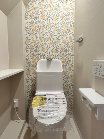 天城通3丁目中古戸建のトイレ|華やかなボタニカル柄のアクセントクロスが目を引く空間。棚板などの細かな配慮も魅力です。
