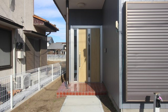 小山市羽川の玄関|明るい木目調の玄関ドアが印象的なエントランスです。屋根付きのアプローチで雨の日も安心。新しい外壁との相性も良く、すっきりとした印象の玄関まわりになっています！