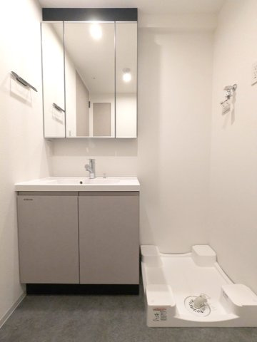OPEN BLOOM入谷Eastの洗面所|トイレと独立した三面鏡付・ハンドシャワー付洗面台、洗濯機置場は排水溝のお手入れをしやすく手前中央に配置し、足高の防水パンです