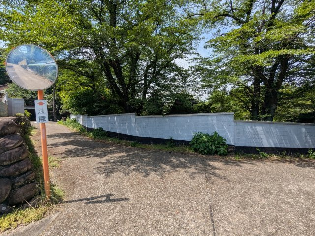 中古戸建　中里見町井ノ下の前面道路含む現地写真|カーブミラーが設置された安心のアクセス。木々の緑と長い白い塀が風情を感じさせる落ち着いた環境です。(