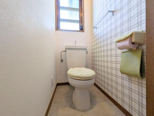 けやき台二丁目　中古のトイレ|窓付きで明るいトイレです。壁面にはチェック柄のクロスが施されています。ペーパーホルダーとタオル掛けが設置されています。トイレマットと便座カバーも付いており清潔感があります。