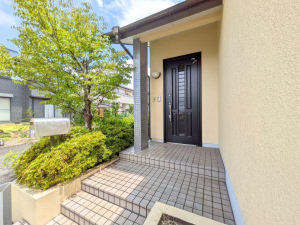 けやき台二丁目　中古の玄関|落ち着いた色合いの外壁と調和した玄関です。タイル張りの階段が玄関までのアプローチを演出しています。植栽やポストが玄関まわりに配置されています。屋根付きの玄関で天候に左右されにくい設計です。