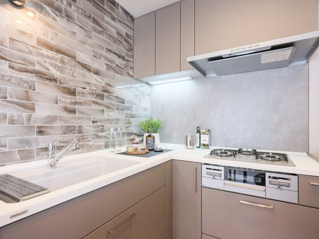 東京八重洲アムフラットのキッチン|快適な機能が充実したシステムキッチンです。石の流れ目と仄かに煌めく表面の石調タイルが、より一層気品溢れる空間を演出します。お部屋の雰囲気に調和した色合いで、さらにランクアップした空間に仕上げました。