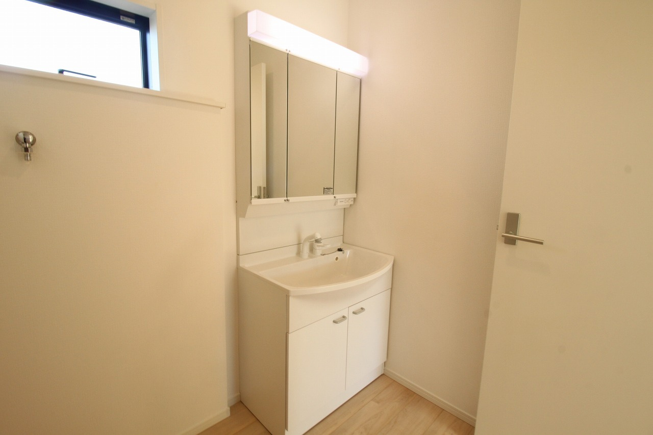 南国市大そね甲第1　新築戸建　1号棟　の独立洗面台|シャワー付洗面化粧台は、寝癖直しや忙しい朝の身支度に大変重宝します。三面鏡の裏側は収納スペースになっており、散らかりがちな洗面小物もスッキリと片付けられ、清潔感のあるサニタリー空間を維持できます。