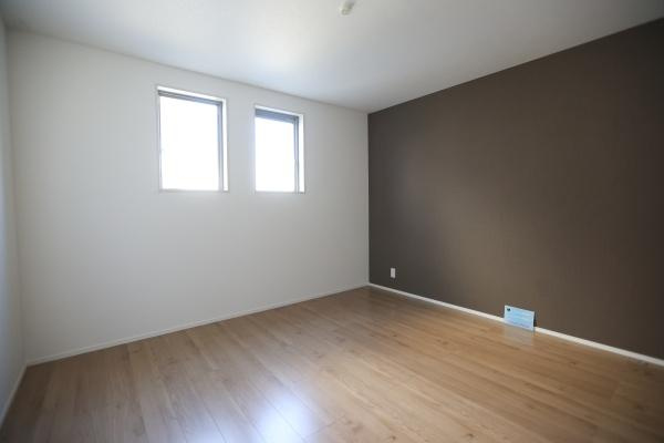 大字森町4期1号棟の洋室|二つの窓から自然光がしっかり差し込む洋室です。落ち着いた色合いのアクセントクロスが特徴です。床には木目調のフローリングが採用されています。すっきりとした内装で家具の配置も考えやすい空間です。