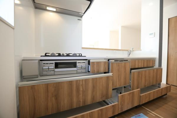 大字森町4期1号棟のキッチン|木目調の面材が特徴的なキッチンです。引き出し収納が充実しており調理道具や日用品もまとめて整理できます。ガスコンロや換気フードも備わっていて使い勝手を考慮した設計です。