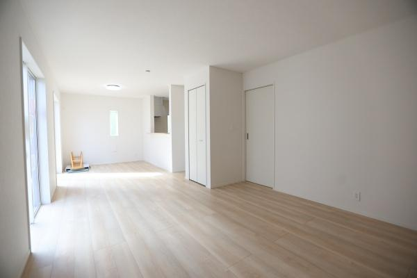 荏隈第3-2号棟の居間・リビング|明るいフローリングが印象的なリビングです。白を基調とした内装でシンプルな空間が広がっています。窓からの自然光がたっぷり入る設計です。収納スペースも充実し使い勝手に配慮されています。