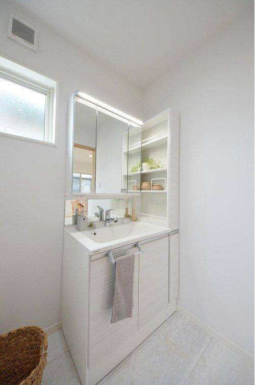 新庄町の洗面所|清潔感あふれる白を基調としたシャワー付洗面台と洗面室。収納もある余裕のスペース。窓もあり明るく通気も良いです。