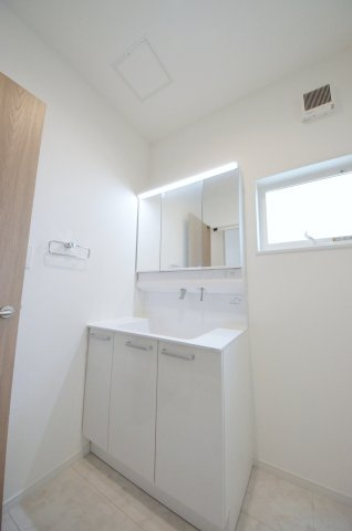古江東町の洗面所|清潔感あふれる白を基調としたシャワー付洗面台と洗面室。収納棚もある余裕のスペース。窓もあり明るく通気も良いです。