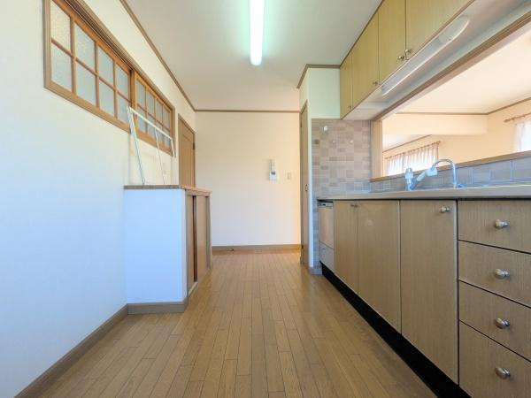 望みが丘　中古のキッチン|明るい日差しが差し込むキッチンスペースです。壁面には収納棚が備え付けられており片付けに便利です。窓が配置されているため換気もしやすい設計です。床は落ち着いた木目調で統一されています。