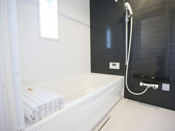 久原中央第4-1号棟の浴室|バスルームは白とダークカラーのバランスが際立っています。小窓からの自然光で空間が明るく感じられます。浴室乾燥機やシャワーヘッドも備わっています。壁面パネルが清潔感を感じさせます。