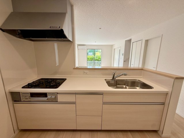 クレイドルガーデン那覇市具志 第４・１号棟のキッチン|レンジフード＆ガスコンロ３口＆浄水器付きキッチンの流し台／リビングの眺め