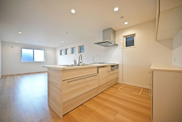 マドレコート甲南台新築一戸建て|4LDK+駐車2台可(車種制限有)のキッチン|1階LDKをキッチンユニット越しに撮影した内観写真です。フルフラットの対面式オープンキッチンを採用しているため視界は広く、ご家族間やご来訪者とのコミュニケーションも一体的に取り易くなっております。