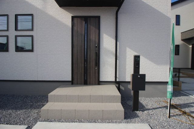 グラファーレ　下野市仁良川　2期　2号棟の玄関|落ち着いた木目調の玄関ドアが印象的なポーチ。屋根付きで雨の日も出入りしやすく、平屋らしい安心感のある玄関まわりです。シンプルで飽きのこないデザインも魅力です。