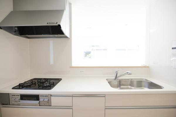 泉町第1-1号棟のキッチン|清潔感のあるキッチンはシンプルなデザインで毎日のお手入れがしやすいです。窓があり明るさも十分に確保されています。三口コンロとシンクが使いやすい配置で調理スペースも広々としています。