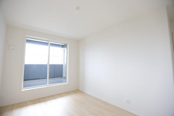 寒田北町第1-2号棟の洋室|明るい色合いのフローリングが特徴の洋室です。大きな窓から光が差し込み開放感があります。シンプルな内装でインテリアを楽しめます。バルコニーへのアクセスも便利です。清潔感のある空間です。