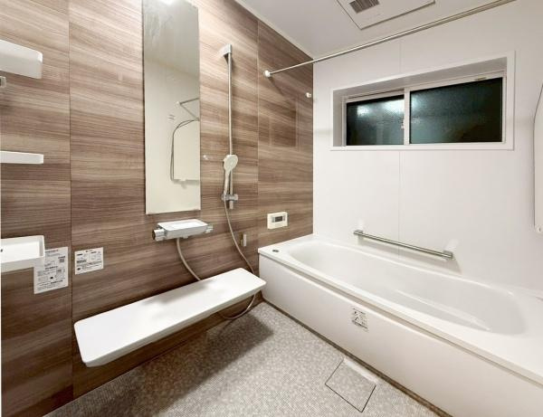 駄原中古の浴室|木目調の壁面が落ち着いた雰囲気を演出しています。大きな鏡とワイドなカウンターが特徴的です。窓付きで換気もしやすく清潔感があります。シンプルなデザインでさまざまなインテリアにも調和します。