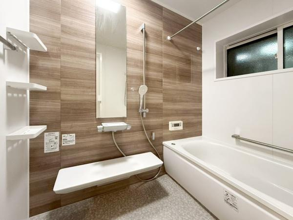 駄原中古の浴室|木目調の壁が洗練された雰囲気を演出しています。大きな鏡と広々としたバスタブが印象的です。収納棚が複数設置されており使いやすさも考えられています。窓付きで換気もしやすいバス空間です。