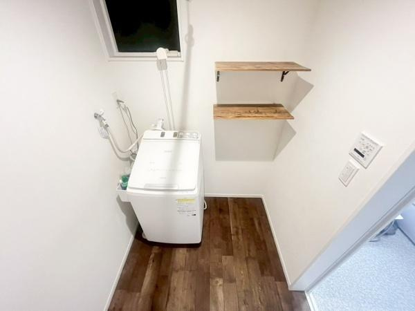 駄原中古の独立洗面台|洗面所には窓があり自然換気がしやすい環境です。洗濯機の設置スペースも確保されています。壁には便利な収納棚があり日用品の整理に役立ちます。床は木目調で落ち着いた印象になっています。