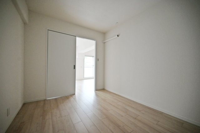サンマンション江坂の洋室|ホワイトの内装に新規で張り替えられたフローリングの木目が映えていますね。長方形の間取りは家具の配置がしやすく、お部屋の模様替えも楽々です。