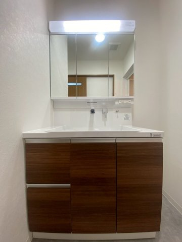 京都市西京区桂南滝川町の洗面所|木目調の扉柄が素敵な洗面化粧台は洗髪のできるシャワーつき。3面鏡タイプで身支度に便利です。