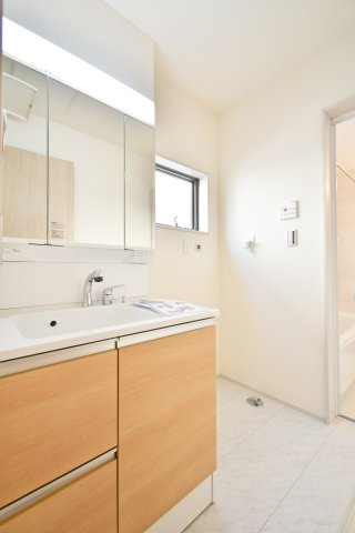 上尾市小敷谷第2全11棟　4号棟の独立洗面台|忙しい朝も快適な三面鏡付きの独立洗面台。鏡の裏は収納になっており、散らかりがちな小物もスッキリ収まります。木目調のパネルが空間を温かく演出し、窓からの通風で湿気対策も可能な洗面室です。