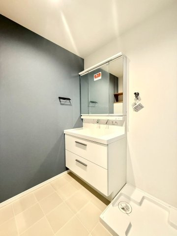 ガーデン南山手の洗面所|白を基調にグレーのアクセントクロスを合わせた洗面空間。三面鏡収納と引き出し収納で使いやすく、清潔感のあるデザインです。