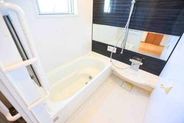 角子原　戸建ての浴室|ゆったりとした浴槽が特徴のバスルームです。手すりが設置されており安全面にも配慮されています。壁面には大きな鏡が備わっていて空間を広く見せてくれます。シンプルなデザインで清潔感があります。