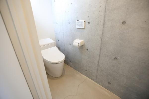 青葉台　戸建てのトイレ|シンプルなデザインとコンクリート打ちっぱなしの壁が印象的なトイレです。無駄のない空間が広がり清潔感を感じられる仕様です。トイレットペーパーホルダーや操作パネルも配置されています。